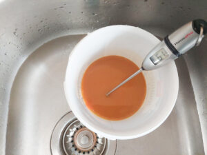 Lye for making soap in a plastic container; a thermometer is in the container and the container is in the sink