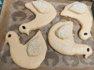 Raw Saint Martin's geese on a baking tray with raisins as eyes and the wings sprinkled with pearl sugar