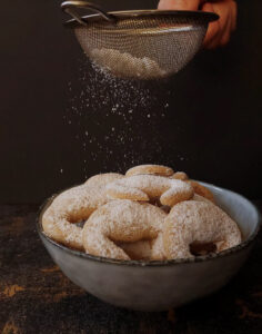 Bowl with Christmas cookies being sprinkled with powdered sugar from above