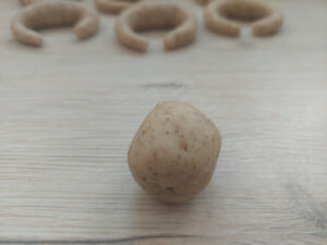 A small ball of cookie dough; in the background ready-bent Vanillekipferl