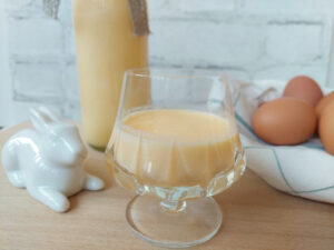 Eierlikör in a glass, eggs, a bottle of Eierlikör and a porcelain rabbit in the background