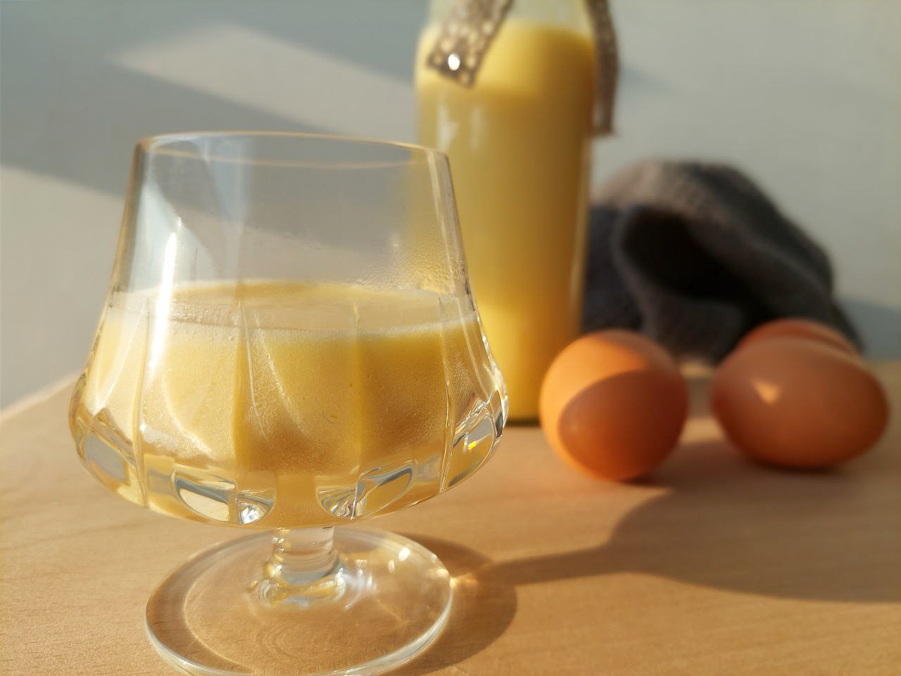 Eierlikör in a glass, eggs and a bottle of Eierlikör in the background