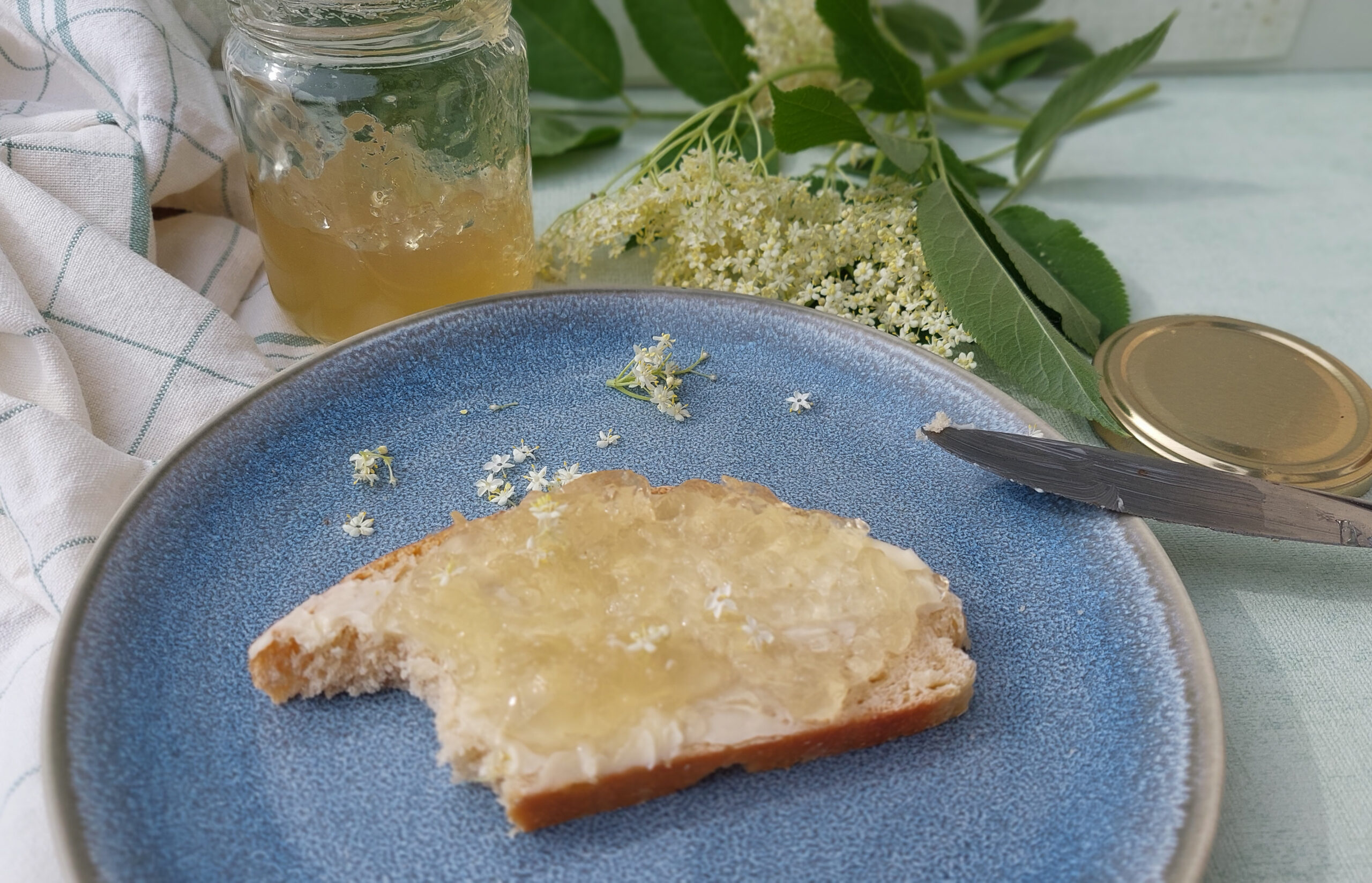 Elderflower jelly on bread, jar and flowers in the background