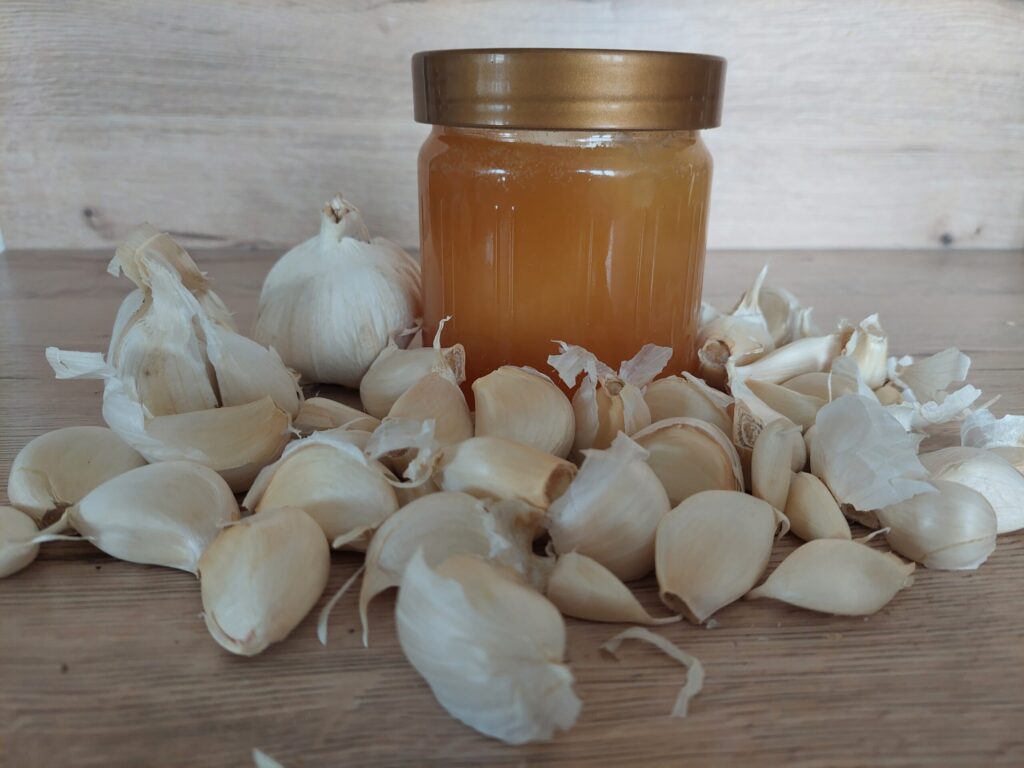 A jar of raw honey, surrounded by garlic cloves