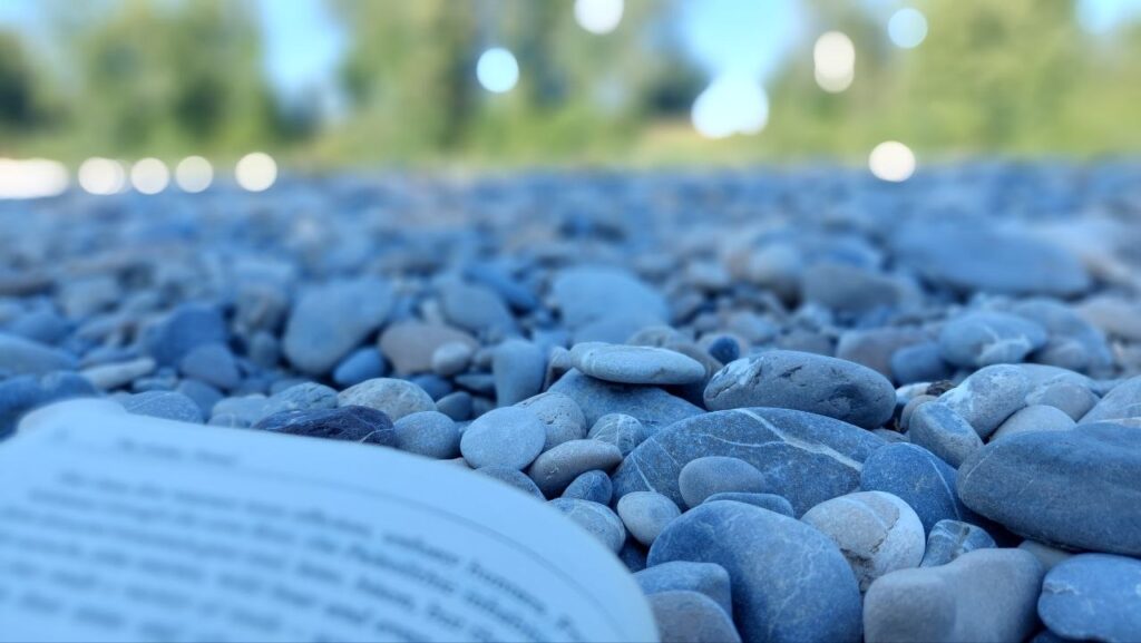 Stone pebbles on the river Lech in summer, an open book in the foreground