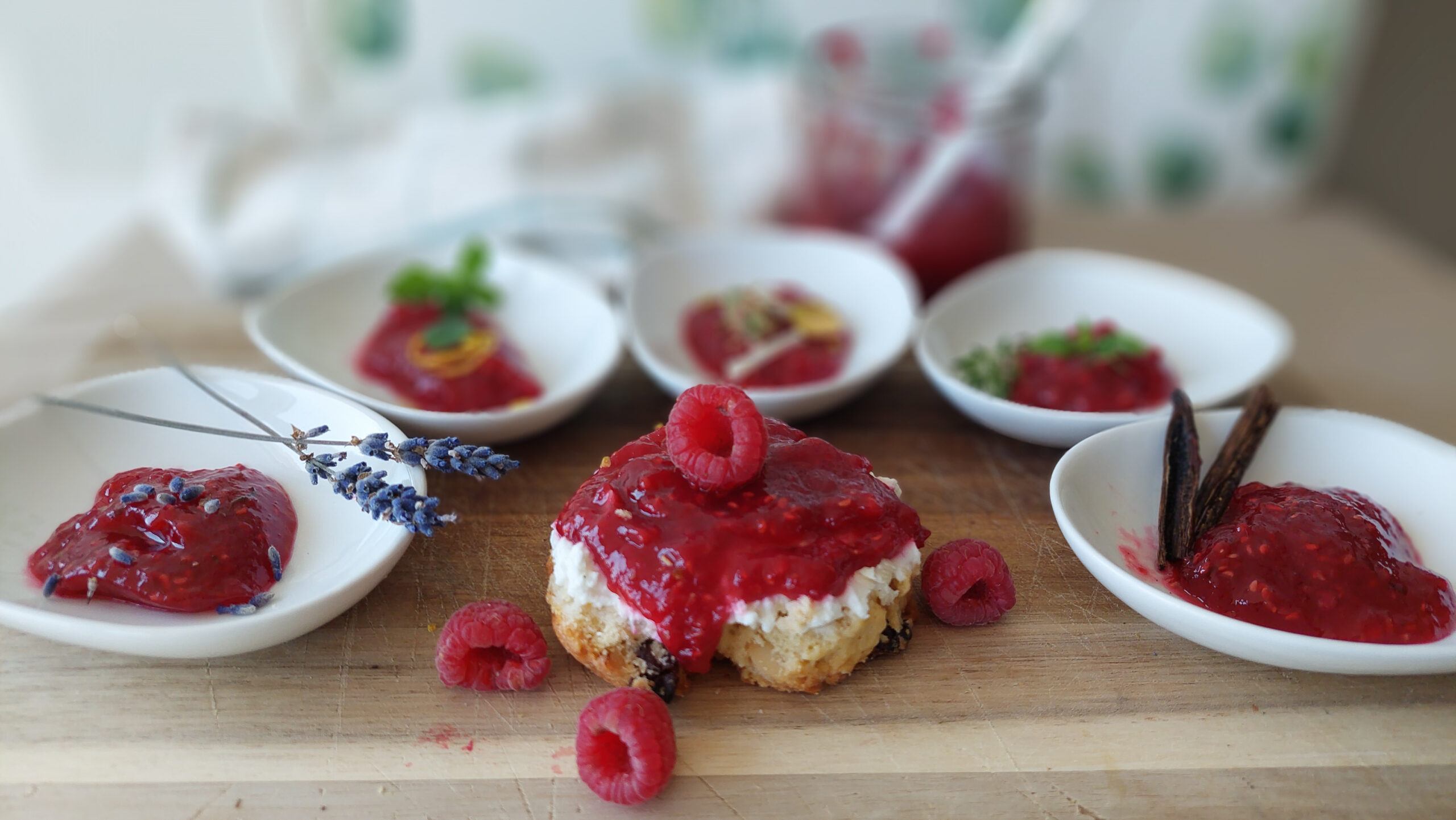 raspberry jams Five dishes with differently flavoured raspberry jams in a half circle, a scone with raspberry jam and a berry on top in the foreground