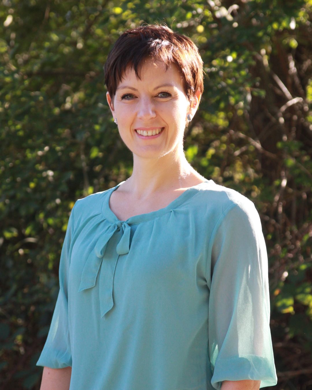 Angela Braun, the founder of Seasonal Simple Life in front of a green bush in the garden